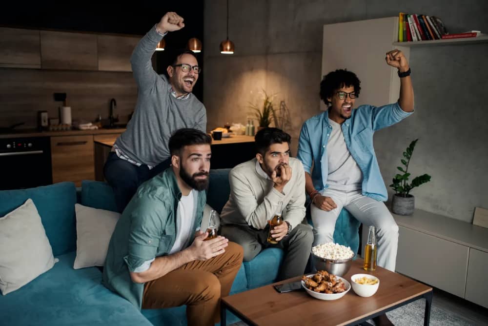 Group of friends celebrating while watching a sports game on television, symbolizing Boxing Day sports fixtures.