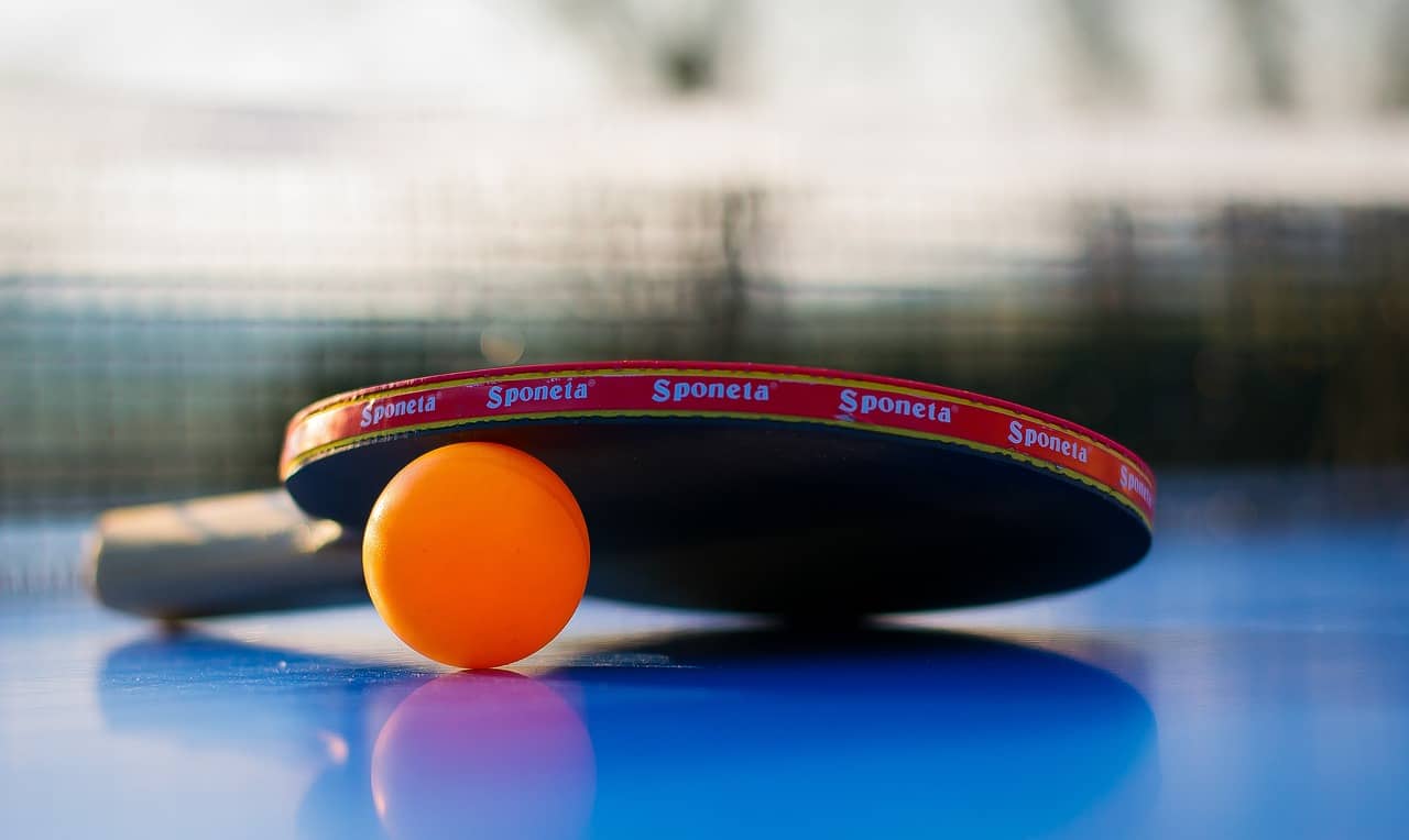 A professional table tennis racket and orange ball on a blue table, representing the ITTF World Team Table Tennis Championships Finals in Busan.