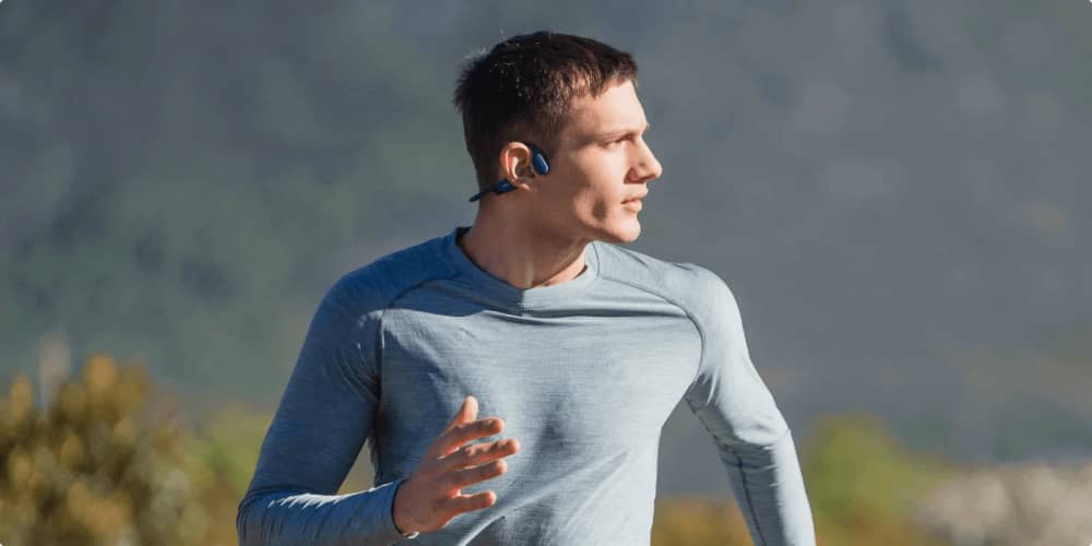Runner wearing blue ergonomic running headphones focused on his outdoor workout.